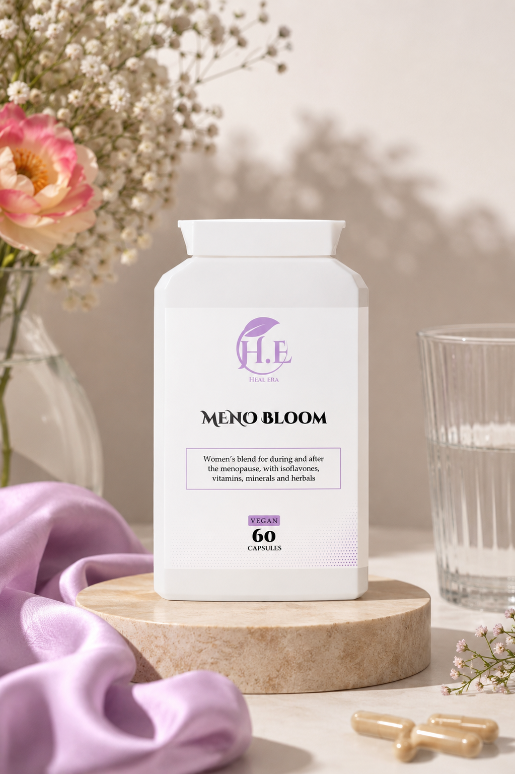 A white bottle of H.E MENO BLOOM dietary supplement capsules displayed on a wooden pedestal, surrounded by soft lavender fabric, dried flowers, and a glass of water.