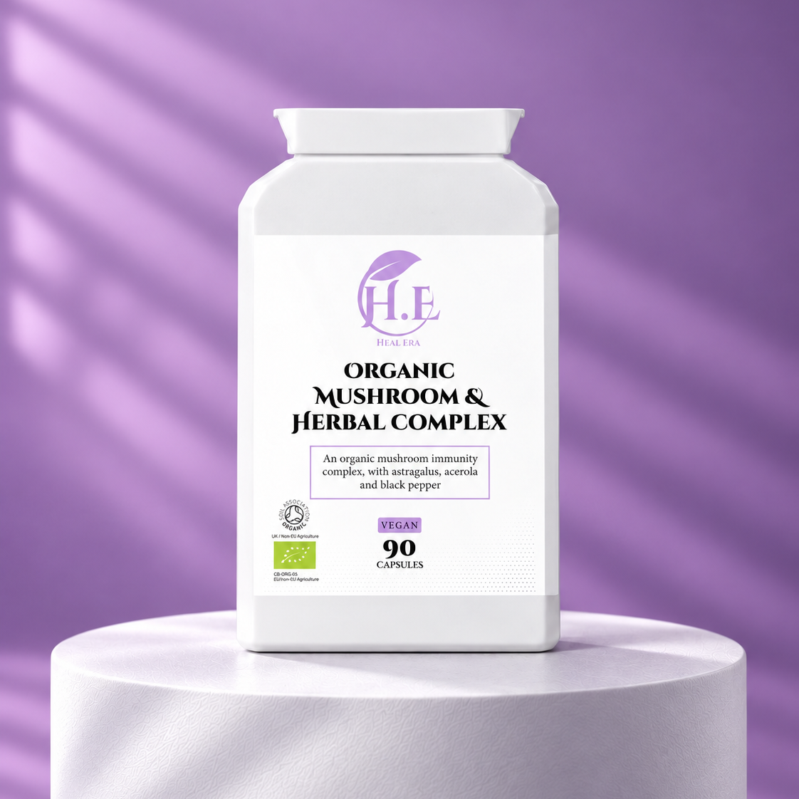 A white bottle of H.E Digital Organic Mushroom & Herbal Complex dietary supplement, displayed on a white cylindrical pedestal against a purple background with soft diagonal shadows.